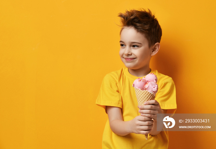 Baby boy kid eating strawberry ice-cream in waffles cone happy screaming laughing on yellow background