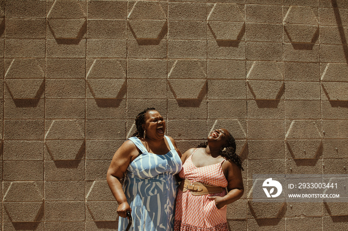 2 plus size African American women stand against a wall laughing