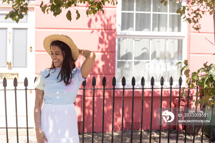 Smiling young woman in sun hat standing in street