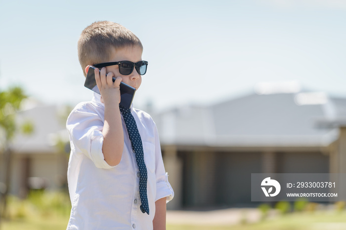 Boy standing and talking on the mobile phone while wearing business attire with sunglasses on a bright summer day