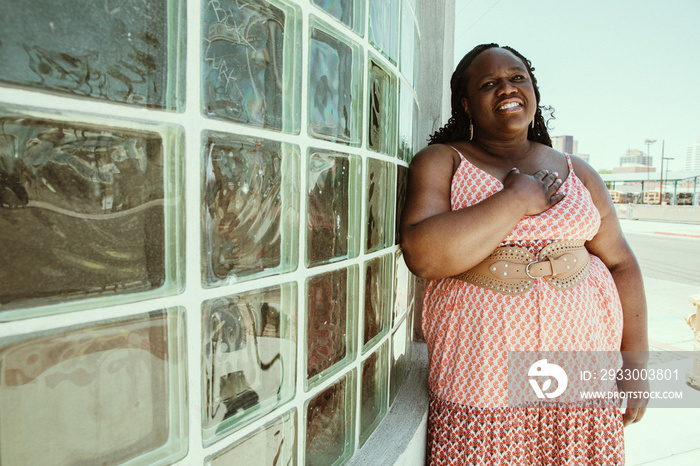 African American woman stands against window with hand on chest