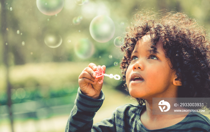 Happy little kid blowing soap bubble in school garden. Child outdoor activity concept.