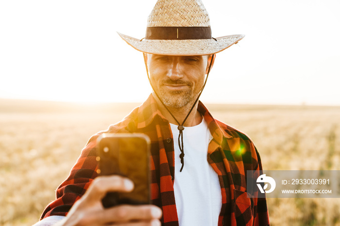 Image of pleased adult man in straw hat taking selfie on mobile phone