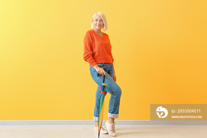 Stylish mature woman with umbrella against color wall