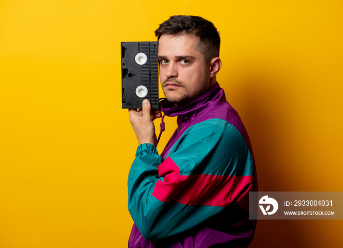 Style man in 90s tracksuit with VHS cassette on yellow background