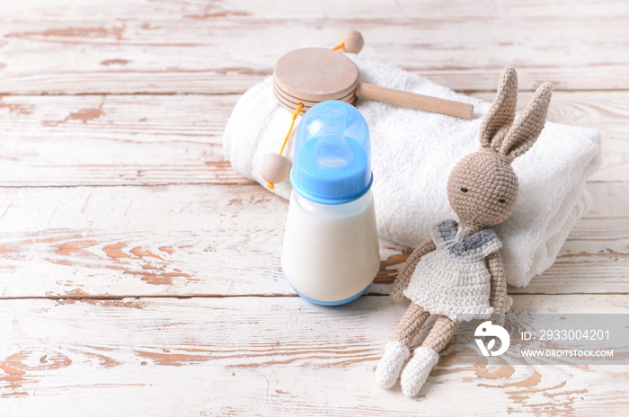 Bottle of milk for baby with toys and towel on white wooden background