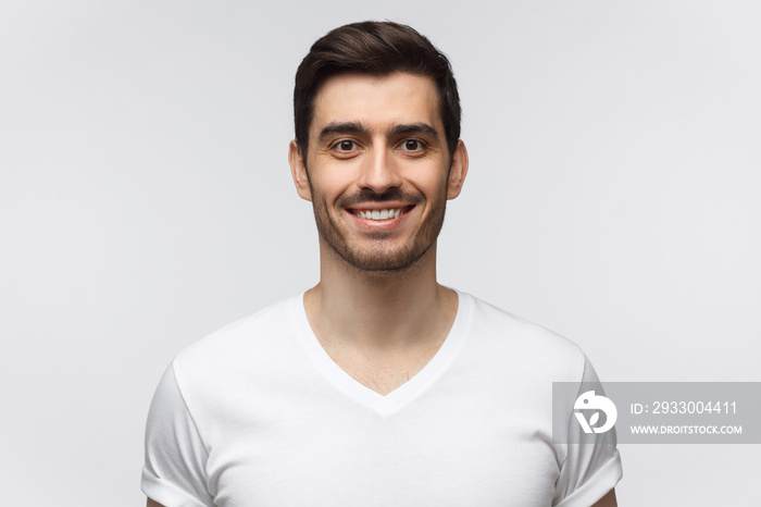 Portrait of smiling handsome young man in white t-shirt looking at camera, isolated on gray background