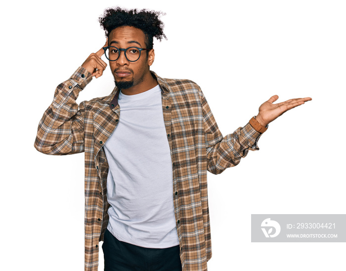 Young african american man with beard wearing casual clothes and glasses confused and annoyed with open palm showing copy space and pointing finger to forehead. think about it.