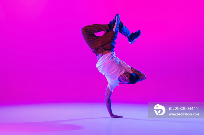 Young stylish man, hip-hop dancer dancing solo in modern clothes isolated over bright magenta background at dance hall in neon light.