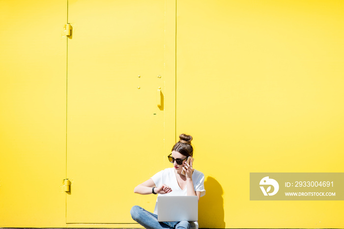 Woman working with laptop on the yellow wall background