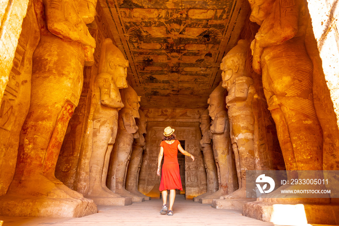 A young woman in red dress looking at the pharaohs at the Abu Simbel Temple in southern Egypt in Nubia next to Lake Nasser. Temple of Pharaoh Ramses II, travel lifestyle