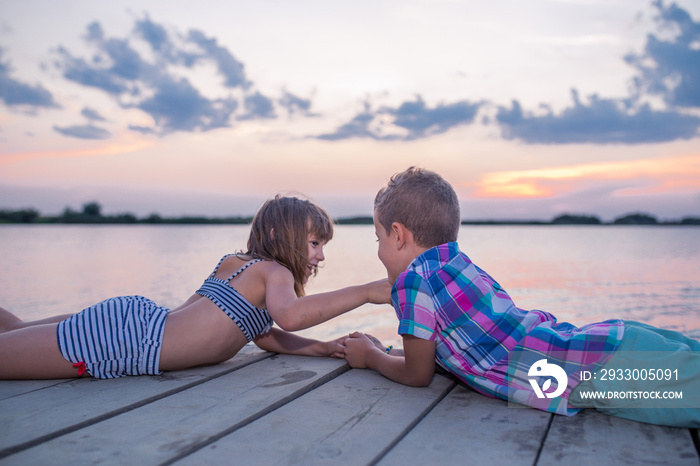 Children lying on the wooden pier and holding hands