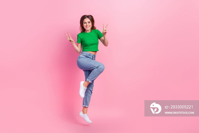 Full length photo of cute excited lady dressed green t-shirt jumping high showing v-signs empty space isolated pink color background