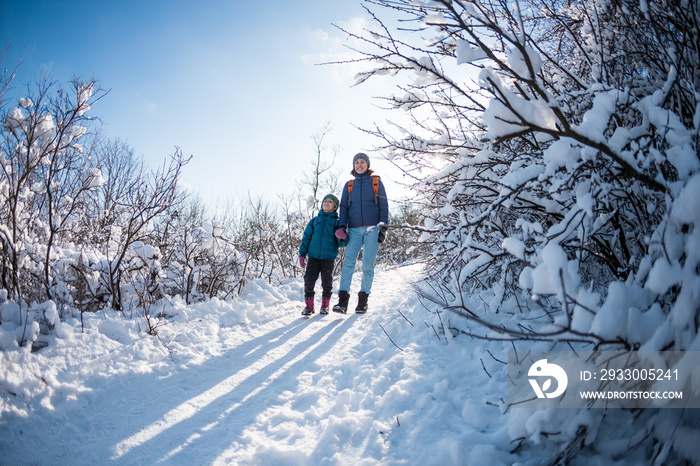 A child with a backpack walks with mother in a snowy forest