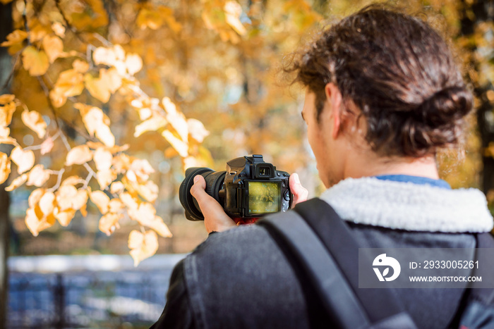 Back view of blogger vlogger video shooter filming colorful autumn park on his camera. Concept of autumn photo or video shootout