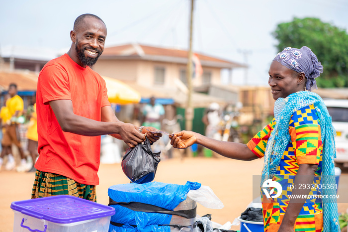 image of cheerful african guy, with Ghana cedi note in his hand, woman with head gear in front- trading concept