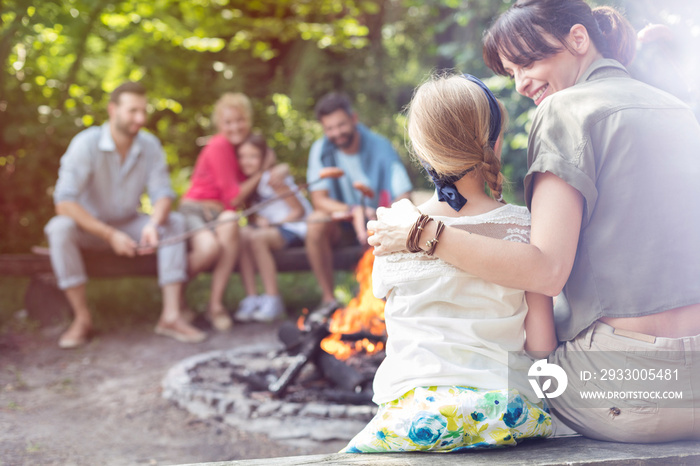 Rear view of mother sitting with arm around daughter while camping at park