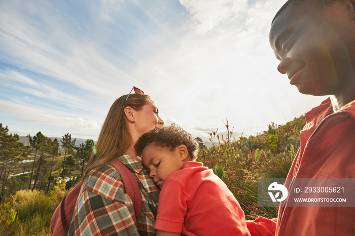 Child resting on mom’s shoulder during family hike and golden hour light