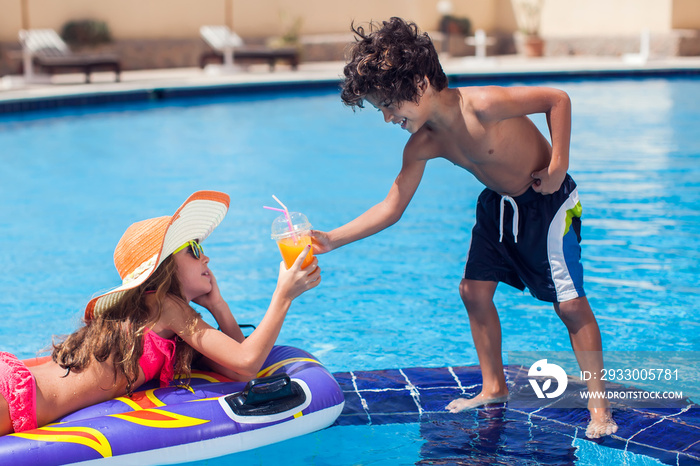 Two kids girl and boy drink juice in the pool and have fun. Children and summer concept