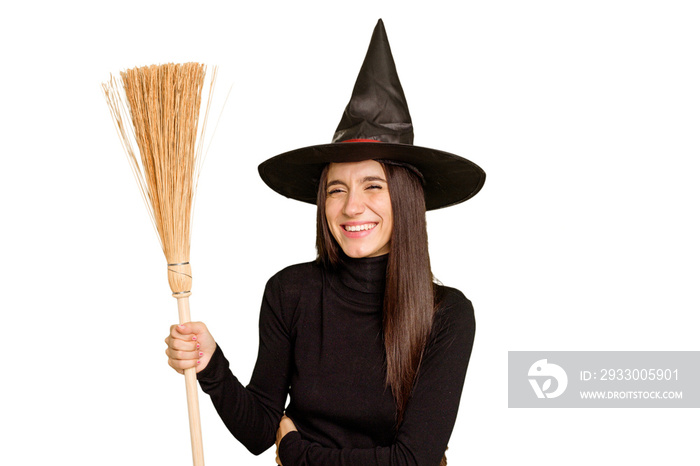 Young caucasian woman dressed as a witch holding a broom isolated laughing and having fun.