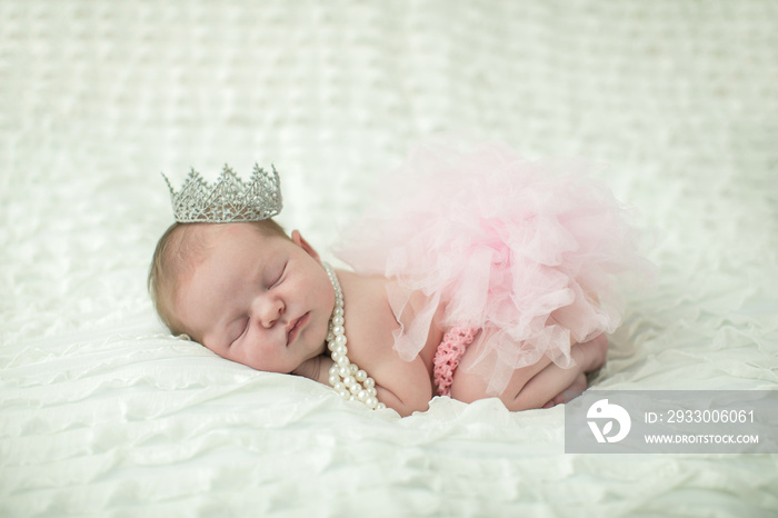Close up of a sweet newborn infant baby girl laying on a cream-colored neutral background with a crown on her head like a little princess royalty. with copy space