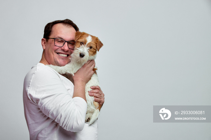 The dog lies on the shoulder of its owner. Jack Russell Terrier in his owner’s hands on white background. The concept of people and animals. T