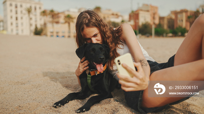 Lunch time. cute girl is sitting on the sand on the beach with her pet testing sandwich. The girl treats her dog with sandwich. Lunch on the beach on modern city background