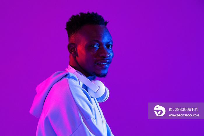 Young handsome African man with headphones in purple futuristic neon light studio background