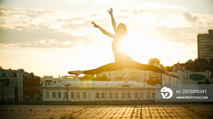 Young woman ballerina jump performing a split on a background of a beautiful bright sunset