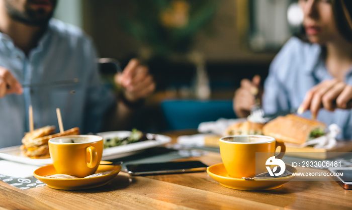 close up shoot of coffee in yellow mug . people eating in blurred background