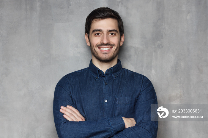 Headshot of Caucasian guy standing with crossed arms and confident look against grey background