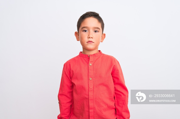 Beautiful kid boy wearing elegant red shirt standing over isolated white background Relaxed with serious expression on face. Simple and natural looking at the camera.