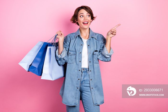 Portrait of cheerful pretty person hold bags look direct finger empty space offer isolated on pink color background