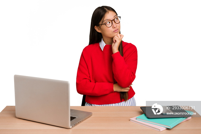 Young student asian woman in a workplace with a laptop isolated thinking and looking up, being reflective, contemplating, having a fantasy.