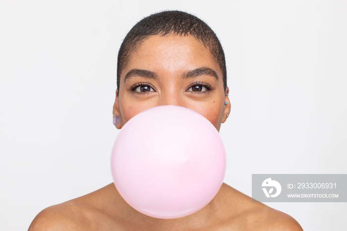 Studio portrait of smiling woman with pink balloon in mouth