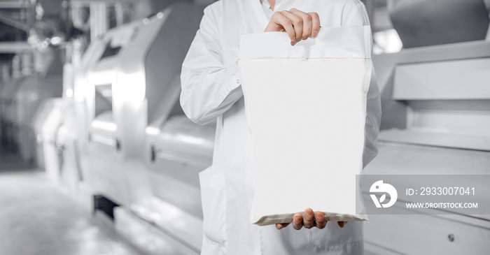 Operator holds bag of flour with products in background of automatic mill for wheat and cereals