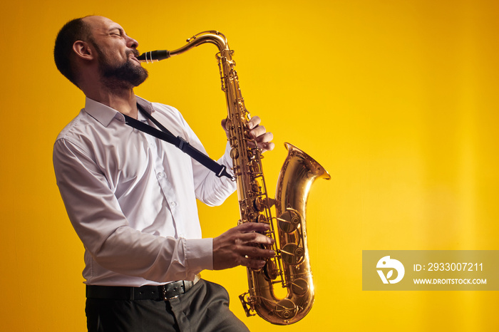 Portrait of professional musician saxophonist man in  white shirt plays jazz music on saxophone, yellow background in a photo studio, side view