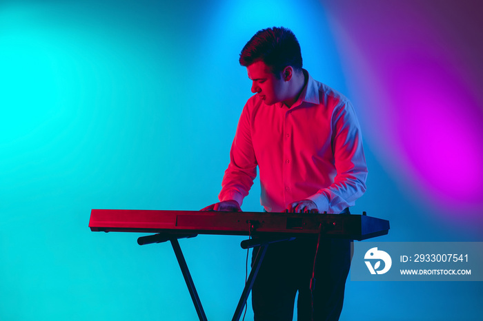 Rhytm accent. Young caucasian inspired and expressive musician, keyboardist performing on multicolored background in neon. Concept of music, hobby, festival, art. Joyful artist, colorful portrait.