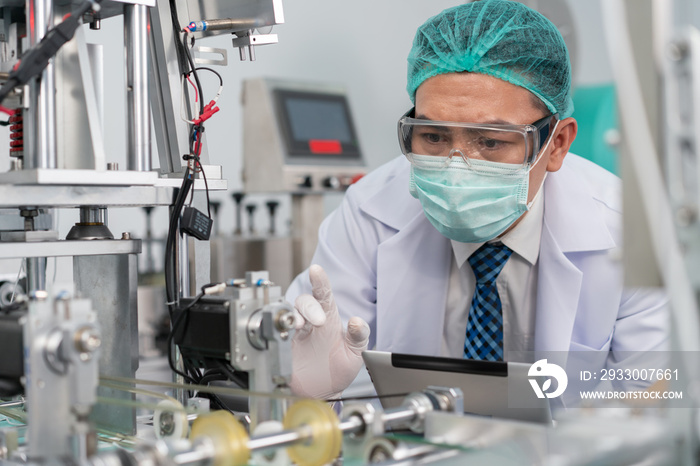 Engineer man wearing hygienic mask to protect coronavirus holding computer tablet checking and inspection machine in production line at factory industry.