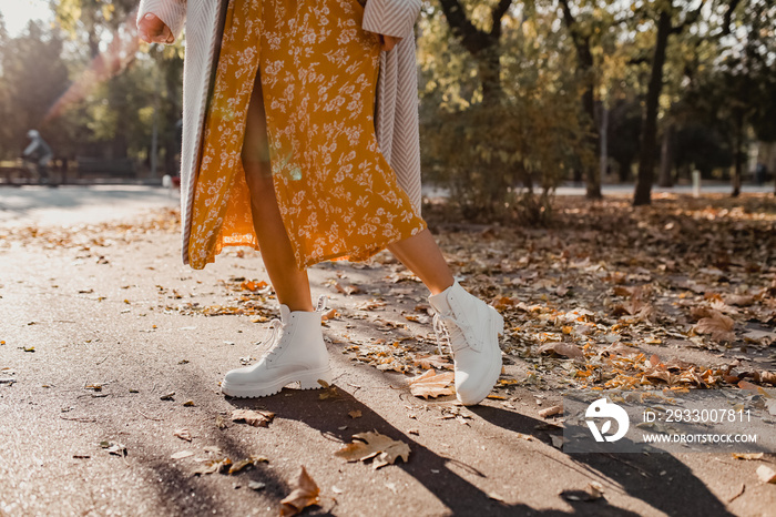 close-up legs in stylish white boots footwear of young woman in yellow printed dress