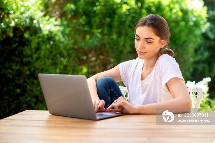 Beautiful young woman using laptop while sitting at desk outdoor