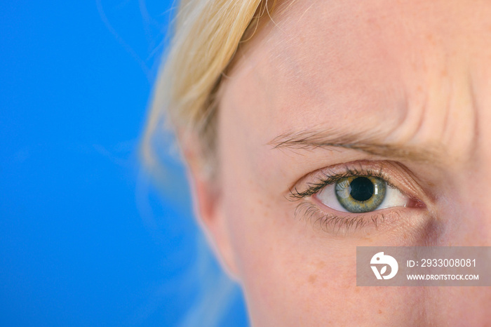 Beautiful blonde woman with clean skin and frekles frown her brows over bright blue background. Thin brows and blue eyes. Thundery brow and sad look.