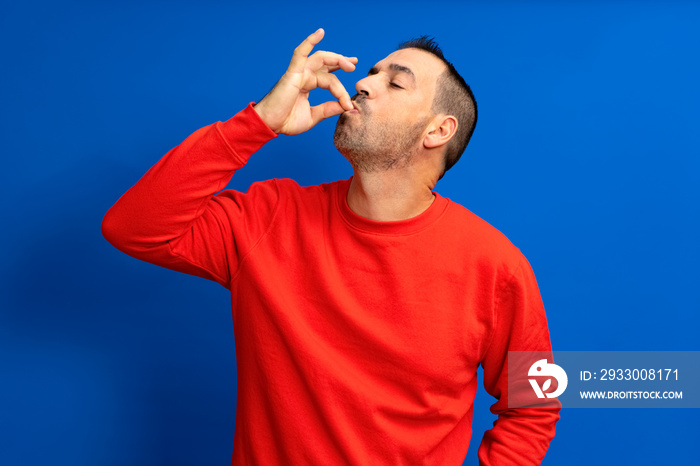 Photo portrait of a man with pursed lips showing gourmet sign with fingers tasty delicious isolated on blue colored background.