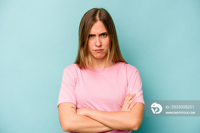 Young caucasian woman isolated on blue background frowning face in displeasure, keeps arms folded.