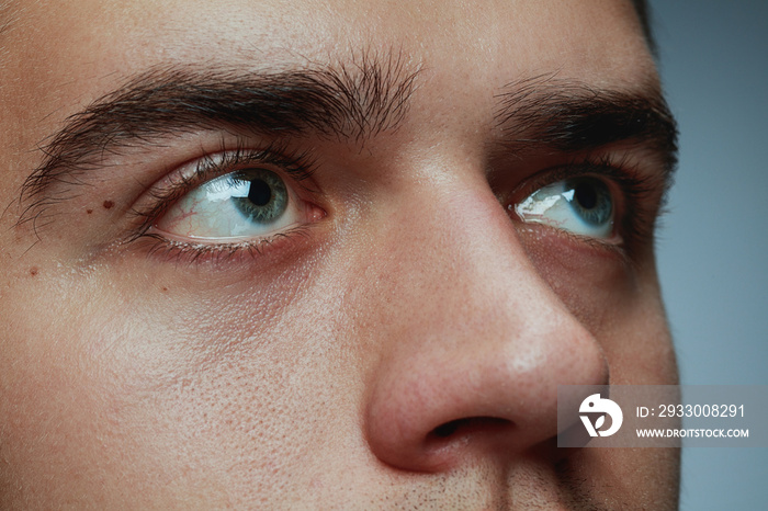 Close-up portrait of young man isolated on grey studio background. Caucasian male model’s face and blue eyes. Concept of men’s health and beauty, self-care, body and skin care, phycology. Looks calm.