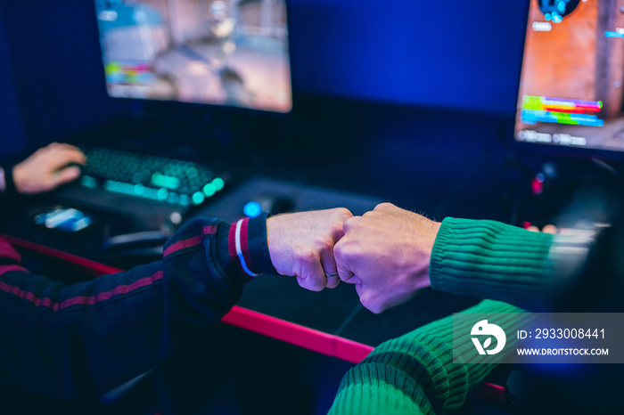 Professional gamer greeting and support team fists hands online game in neon color blur background. Soft focus, back view