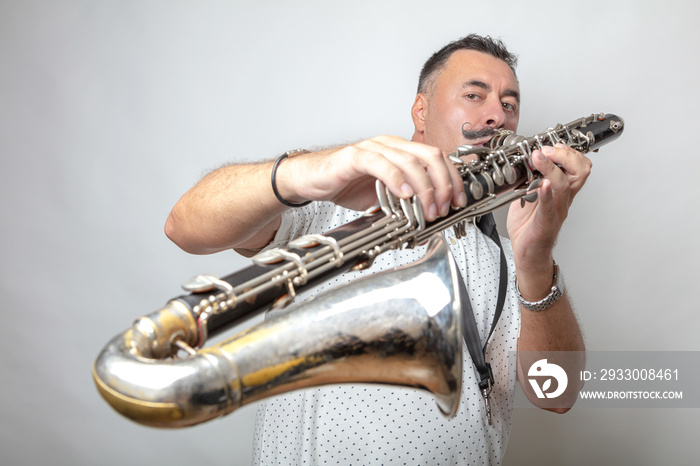 A man, dark, short hair, plays the bass clarinet. Studio, light background