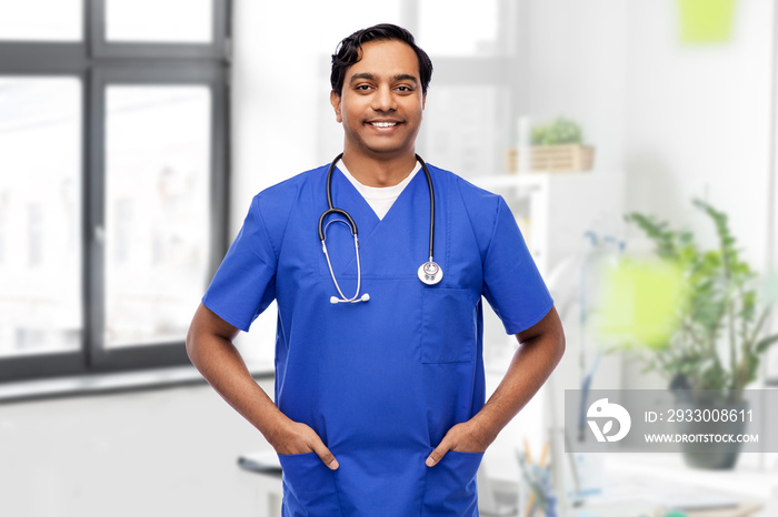 healthcare, profession and medicine concept - happy smiling indian doctor or male nurse in blue uniform with stethoscope over medical office at hospital on background