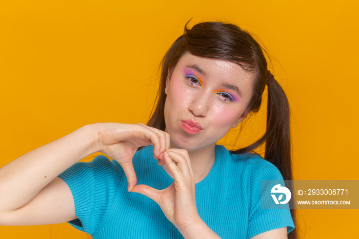 Studio portrait of girl with colorful make-up showing heart shaped gesture