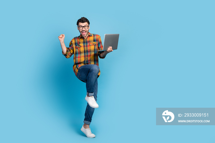 Full body portrait of delighted positive man raise fist achievement triumph hold netbook isolated on blue color background